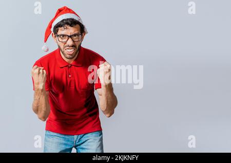 Mann mit Bart und weihnachtsmütze, wütend, wenn er isoliert in die Kamera schaut. Ein wütender weihnachtsmann, der in die Kamera schaut. Menschen mit weihnachtshüten sind wütend und wütend Stockfoto