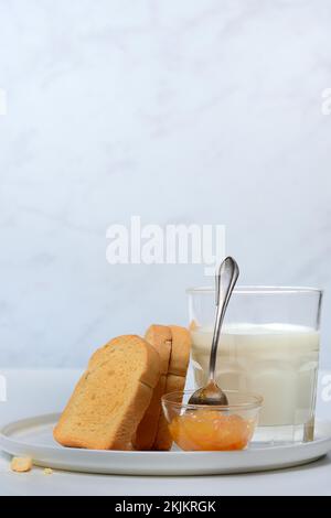 Rusk, ein Glas Milch und Orangenmarmelade in kleinen Schüsseln Stockfoto