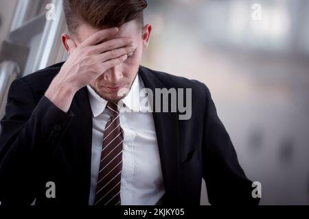 Junger Geschäftsmann mit Kopfschmerzen, müde, überarbeitend, macht Fehler, Stress, Terminations- oder Depressionskonzept. Stockfoto