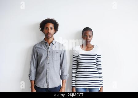 Echter Style. Ein Porträt eines ausdruckslosen jungen Paares, das zusammen an einer weißen Wand steht. Stockfoto