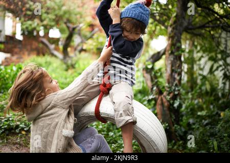 Tarzan und Jane. Zwei süße Kinder, die auf einer Reifenschaukel in ihrem Garten spielen. Stockfoto