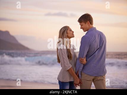 Liebe war nur ein Wort, bis du es bedeutest. Ein glückliches junges Paar, das einen romantischen Moment am Strand bei Sonnenuntergang genießt. Stockfoto