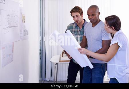 Ich sehe mir die Pläne an. Drei junge Architekten diskutieren Baupläne im Büro. Stockfoto