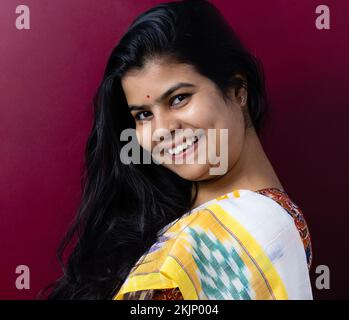 Eine hübsche Indianerin in Saree, die auf farbigem Hintergrund lächelt Stockfoto