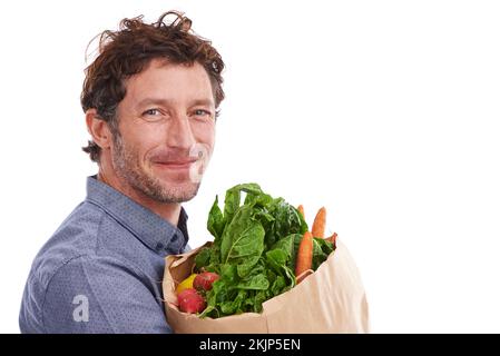 Meine Frau mag es, wenn ich einkaufe. Studiofoto eines gutaussehenden jungen Mannes, der eine Einkaufstasche mit frischem Gemüse hält. Stockfoto