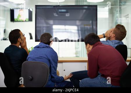 Als Team die Qual der Niederlage zu spüren. Rückansicht einer Gruppe schockierter junger Männer, die einen Montior betrachten. Stockfoto