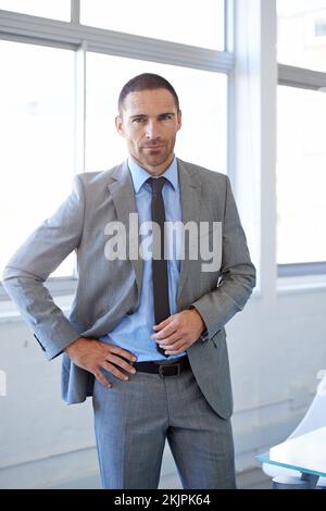 Er ist ein Großunternehmen. Ein gutaussehender Geschäftsmann, der in seinem Büro steht. Stockfoto