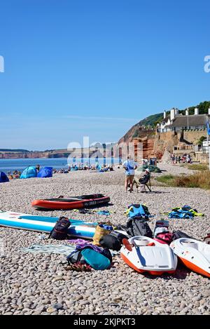 Touristen entspannen sich am Strand mit Blick auf das Meer und die Klippen, Sidmouth, Devon, Großbritannien, Europa. Stockfoto