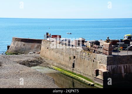 Touristen stehen auf der Hafenmauer am Ende der Promenade mit Blick auf das Meer, Sidmouth, Devon, Großbritannien, Europa. Stockfoto