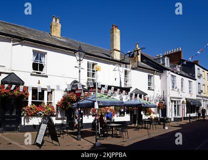 Touristen entspannen sich an Tischen vor dem Anchor Inn entlang der Old Fore Street im Stadtzentrum, Sidmouth, Devon, Großbritannien, Europa. Stockfoto