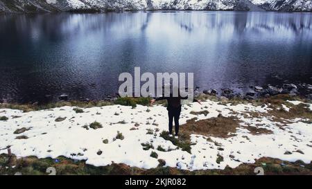 Glückliche Frau, die die Czarny Staw pod Rysamy oder den Black Pond See in der Nähe der Morskie Oko Snowy Mountain Hut in den polnischen Tatry Bergen genießt, Blick auf die Drohne, Zakopane, Polen. Einheit mit Natur Luftaufnahme der wunderschönen grünen Hügel und Berge in dunklen Wolken und Reflexion auf dem See Morskie Oko. Reiseziel 4K Stockfoto