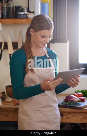 Auswahl des perfekten Rezepts für den Anlass. Eine junge Frau, die auf ihrem digitalen Tablet nach Online-Rezepten sucht. Stockfoto