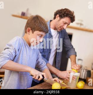 Väter mit der rechten Hand in der Küche. Ein verkürztes Porträt eines glücklichen Vaters und Sohnes, die Limonade in ihrer Küche zuhause machen. Stockfoto