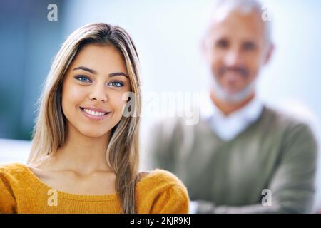 Erfolg bringt uns zum Lächeln. Porträt einer selbstbewussten jungen Geschäftsfrau mit ihrer Kollegin hinter ihr. Stockfoto