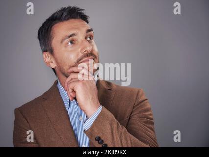 Er denkt sich die Dinge durch. Studiofoto eines Mannes mit tiefem Denken vor grauem Hintergrund. Stockfoto