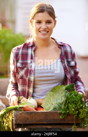 Selbst gebaut ist am gesündesten. Porträt einer glücklichen jungen Frau, die eine Kiste mit frisch gepflücktem Gemüse hält. Stockfoto