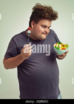 Ich freue mich auf diesen Salat. Studiofoto eines übergewichtigen Mannes mit einer Schüssel Salat. Stockfoto