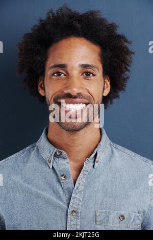 Er hat ein charmantes Lächeln. Porträt eines gutaussehenden jungen Mannes mit einem großen Lächeln auf grauem Hintergrund. Stockfoto