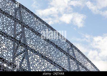 Dekorative Metallwand mit rundem Lochmuster unter wolkenblauem Himmel, abstraktes Hintergrundbild aus der Industrie Stockfoto