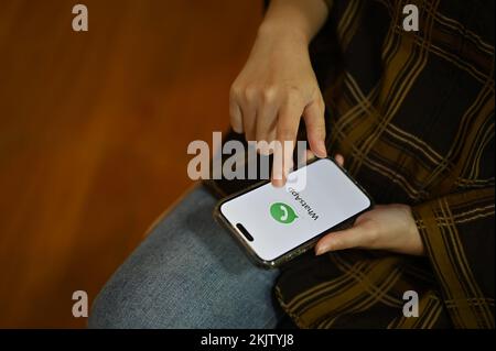 Chiang Mai, Thailand - Nov. 24 2022: Eine weibliche Hand hält ein weißes WhatsApp-Logo auf dem Bildschirm. Mobile Chat-Anwendung. Stockfoto