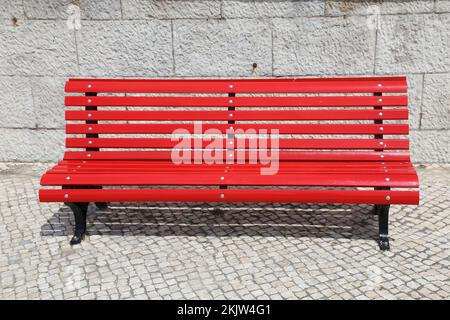 Eine hellrote Parkbank mit Steinwänden. Stockfoto
