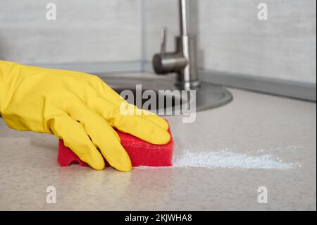 Tiefenreinigung. Frauenhandschuhe Hände putzen Küchentisch mit rotem Schwamm. Oberflächendesinfektion. Hausreinigung und -Desinfektion. Nitril tragen Stockfoto