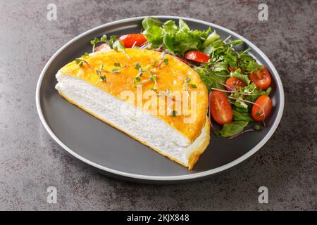 Köstliches französisches Poulard-Omelette mit ausgetretenem Eiweiß und frischem Salat aus nächster Nähe auf einem Teller auf dem Tisch. Horizontal Stockfoto