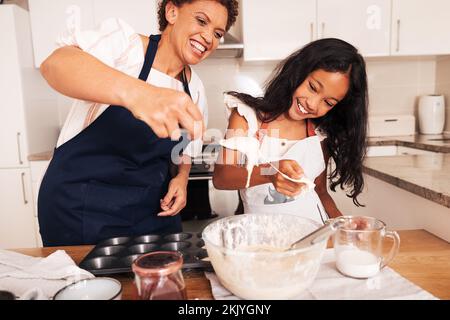 Das Mädchen und ihre Großmutter haben Spaß, während sie Teig in der Küche mixen. Lächelnde Oma und ein Kind, die zusammen kochen. Stockfoto