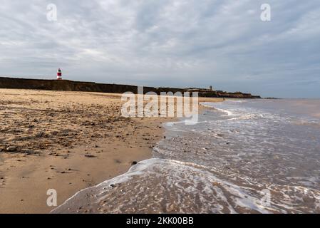 Ein Nachmittagsfoto entlang der Küste von Happisburgh Beach mit Klippen, Leuchtturm und Kirche im Hintergrund - Januar 2021 Stockfoto