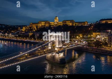 Blick auf den Buda-Palast und die Szechenyi-Kettenbrücke über die Donau bei Abenddämmerung in Budapest, Ungarn. Stockfoto