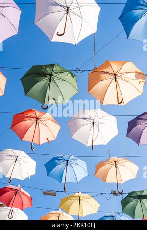 Offene mehrfarbige Regenschirme hängen über dem Durchgang zwischen den Häusern Stockfoto