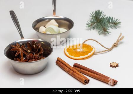 Trockene Orange an der Schnur, Zimtstangen, Fichtenzweig. Marshmallow und Sternanis in Metallschüsseln. Weißer Hintergrund. Stockfoto