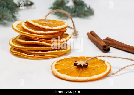 Trockne Orangenscheiben an einer Schnur, Zimtstangen und Fichtenzweigen. Schließen. Weißer Hintergrund. Stockfoto