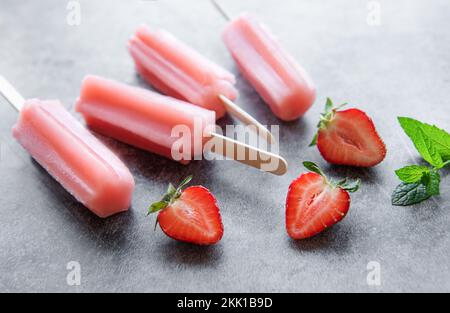 Hausgemachte gefrorene Erdbeer-Eis-Eiszapfen und frische Erdbeeren auf einem betonierten Hintergrund. Sommerdessert Stockfoto