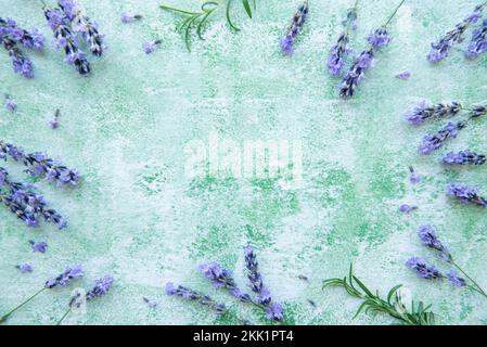 Lavendel blüht und hinterlässt einen kreativen Rahmen auf einem grünen Holzhintergrund. Draufsicht, flach liegend. Florale Komposition Stockfoto