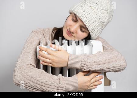 Eine brünette Frau mit Hut umarmt einen Ölwärmer und wärmt sich im Winter auf. Stockfoto