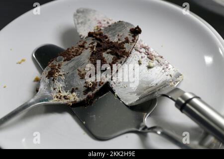 Mehrere dreckige Kuchenbecher auf einem weißen Teller. Diese Kuchenservierwerkzeuge haben viele Kuchenstücke - ungesäubert, noch nicht gewaschen. Stockfoto