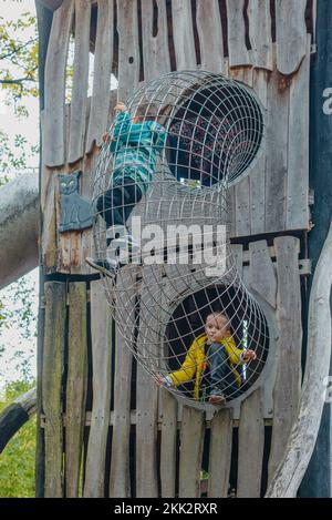 Ein Kind klettert an einem heißen Sommertag in einem Park auf einem Spielplatz auf ein Berggitter. Kinderspielplatz in einem öffentlichen Park, Unterhaltung und Erholung Stockfoto