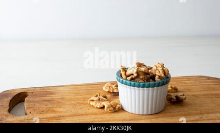 Nahaufnahme einer kleinen weißen Krabbenschüssel mit Walnüssen. Auf einem Holztisch mit weißem Hintergrund platziert Stockfoto