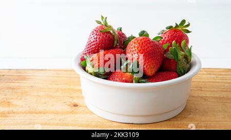 Nahaufnahme einer weißen Keramikschüssel mit roten, frischen Erdbeeren im Inneren auf einem Holztisch Stockfoto