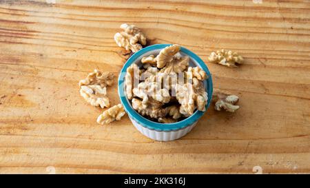 Draufsicht auf eine kleine weiße Krabbenschüssel mit Walnüssen. Auf einem Holztisch mit weißem Hintergrund platziert Stockfoto