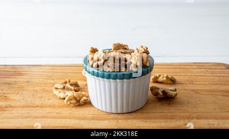 Nahaufnahme einer kleinen weißen Krabbenschüssel mit Walnüssen. Auf einem Holztisch mit weißem Hintergrund platziert Stockfoto