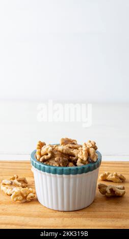 Nahaufnahme einer kleinen weißen Krabbenschüssel mit Walnüssen. Auf einem Holztisch mit weißem Hintergrund platziert Stockfoto