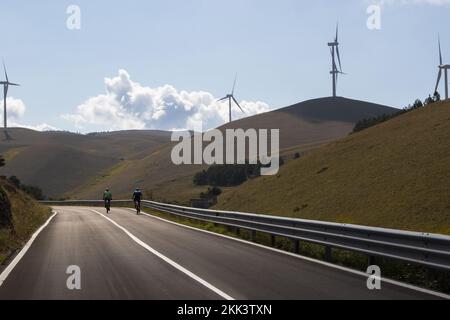 Mann auf dem Fahrrad an einem Tag inmitten der Natur inmitten von Windturbinen in Italien. Nachhaltigkeit zur Unterstützung einer grünen Wirtschaft Stockfoto