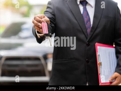 Autoschlüssel, Saleman übergibt den Autoschlüssel auf einen unscharfen Hintergrund. Stockfoto