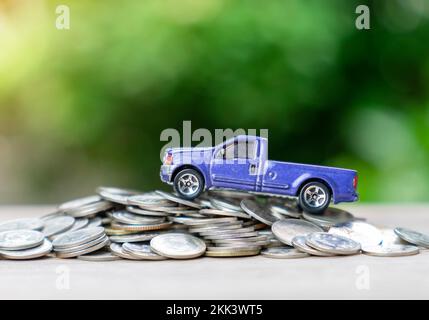 Blaues Pick-up-Car-Modell klettert auf den Geldpflückstapel auf einem unscharfen Hintergrund. Stockfoto