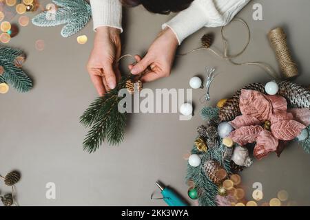 Frau macht Weihnachtskranz, Draufsicht. Blumenhände für festliche Dekoration. Weihnachtskranz-Workshop mit Kopierraum. Draufsicht Stockfoto