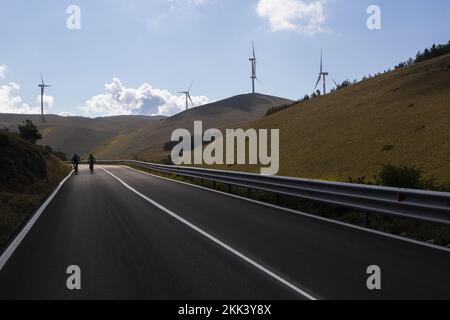 Mann auf dem Fahrrad an einem Tag inmitten der Natur inmitten von Windturbinen in Italien. Nachhaltigkeit zur Unterstützung einer grünen Wirtschaft Stockfoto