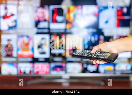 Fernbedienung in der Hand. Smart TV im Hintergrund und Content-on-Demand-Konzept. Stockfoto