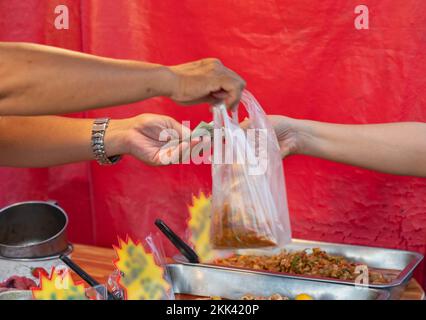 Die Hand einer Frau, die Geld in der Hand hält, kauft Straßenküche auf rotem Leinwand. Stockfoto